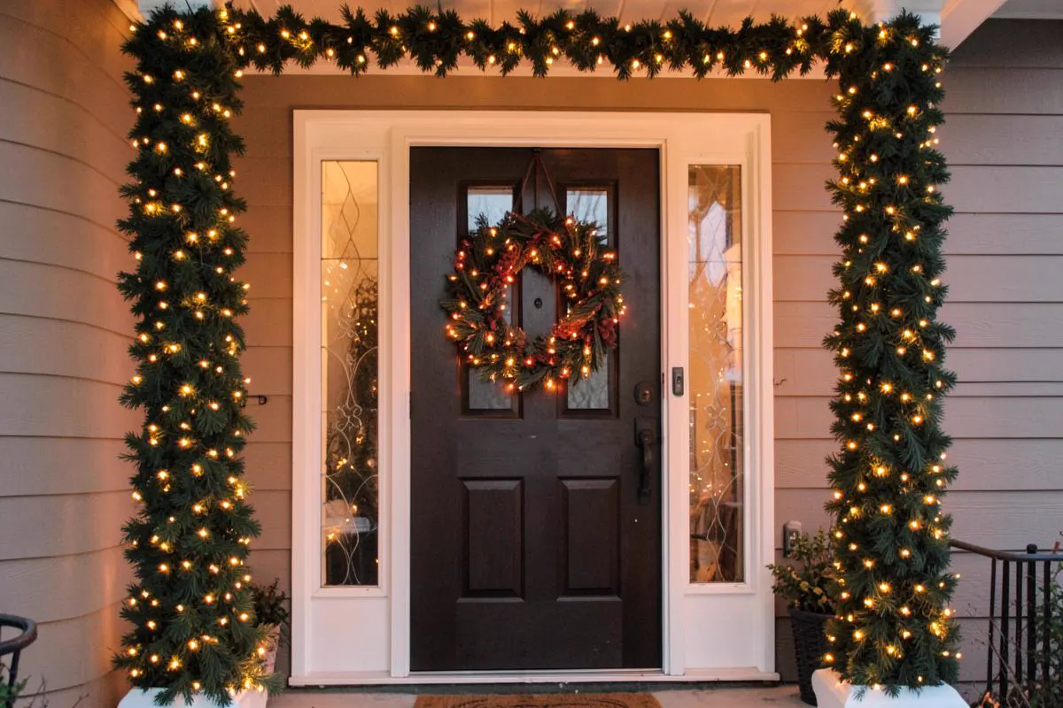 Lit garland wrapped around porch columns with a door wreath