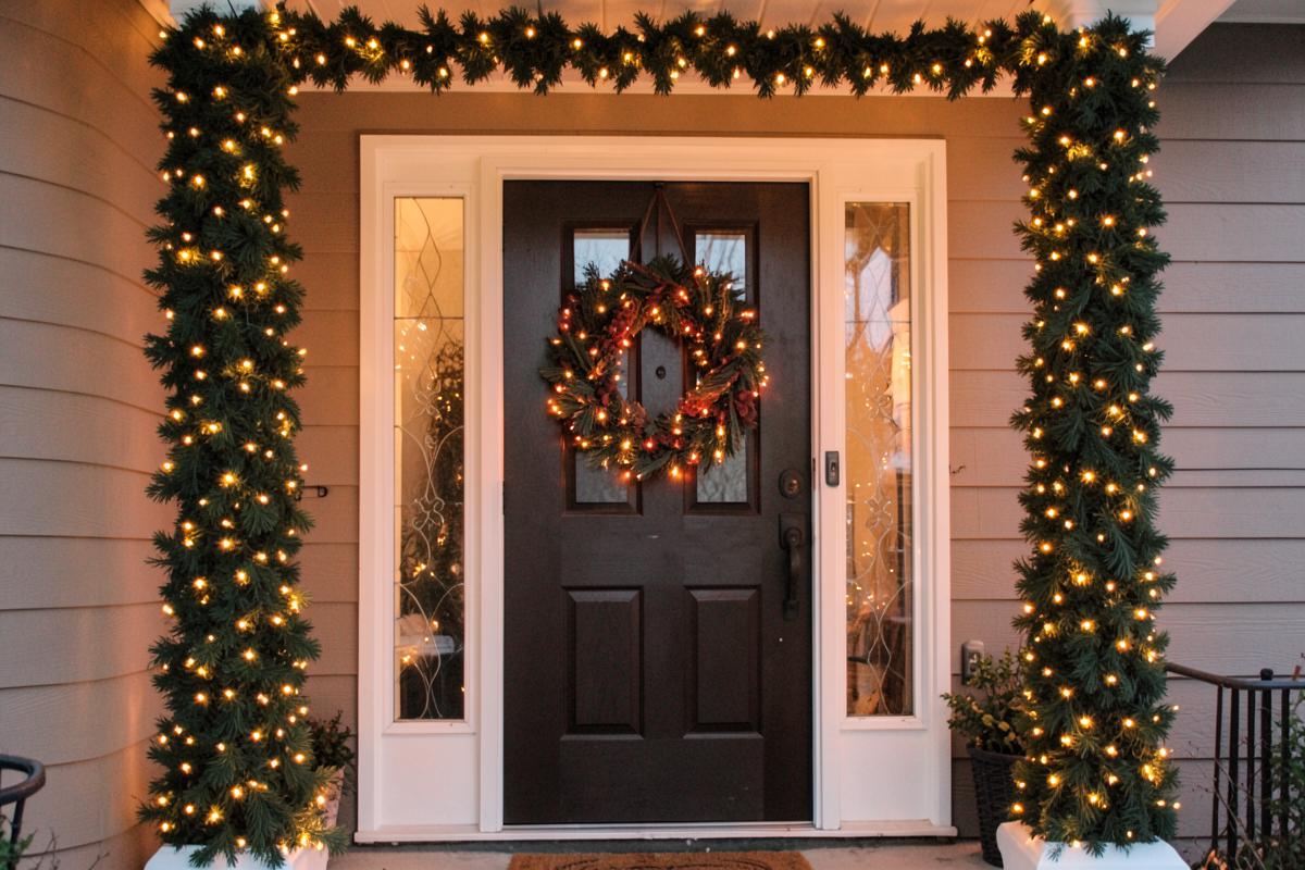 Lit garland wrapped around porch columns with a door wreath